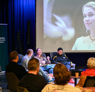 Paneldiskusjon med publikum som ser på en stor projeksjon av en smilende blond kvinne. Banneren indikerer en kulturell begivenhet i Norge.