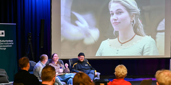 Paneldiskusjon med publikum som ser på en stor projeksjon av en smilende blond kvinne. Banneren indikerer en kulturell begivenhet i Norge.
