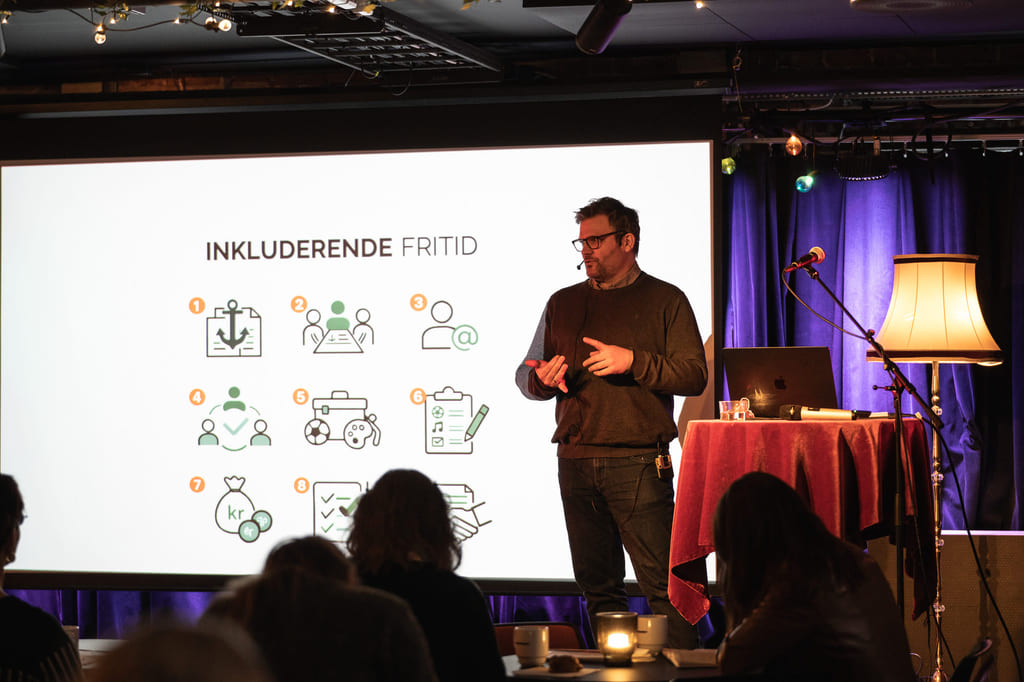 Presentasjon med illustrasjoner om inkludering og foredragsholder på scene.