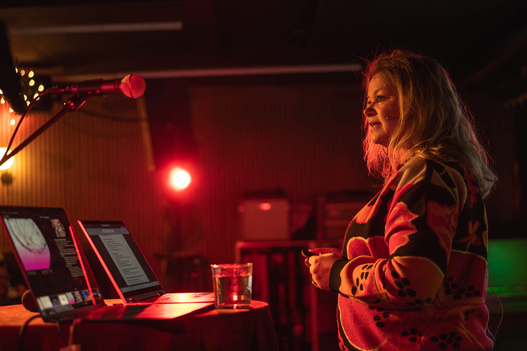 Foredragsholder på scene med lyssetting i røde toner.