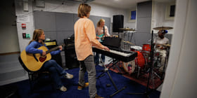 Fire ungdommer spiller på ulike instrumenter i et øvingslokale.