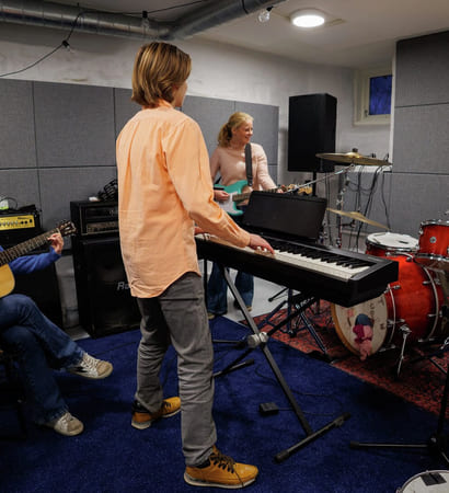 Fire ungdommer spiller på ulike instrumenter i et øvingslokale.