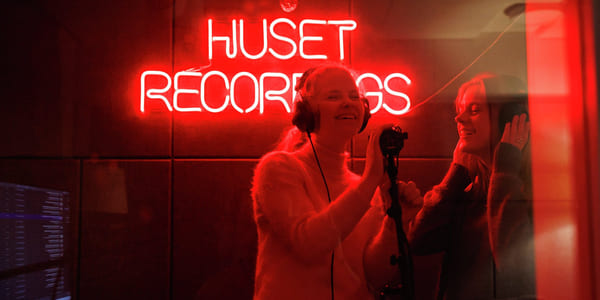 To personer i et innspillingsstudio foran et rødt neonskilt som sier «HUSET RECORDINGS».