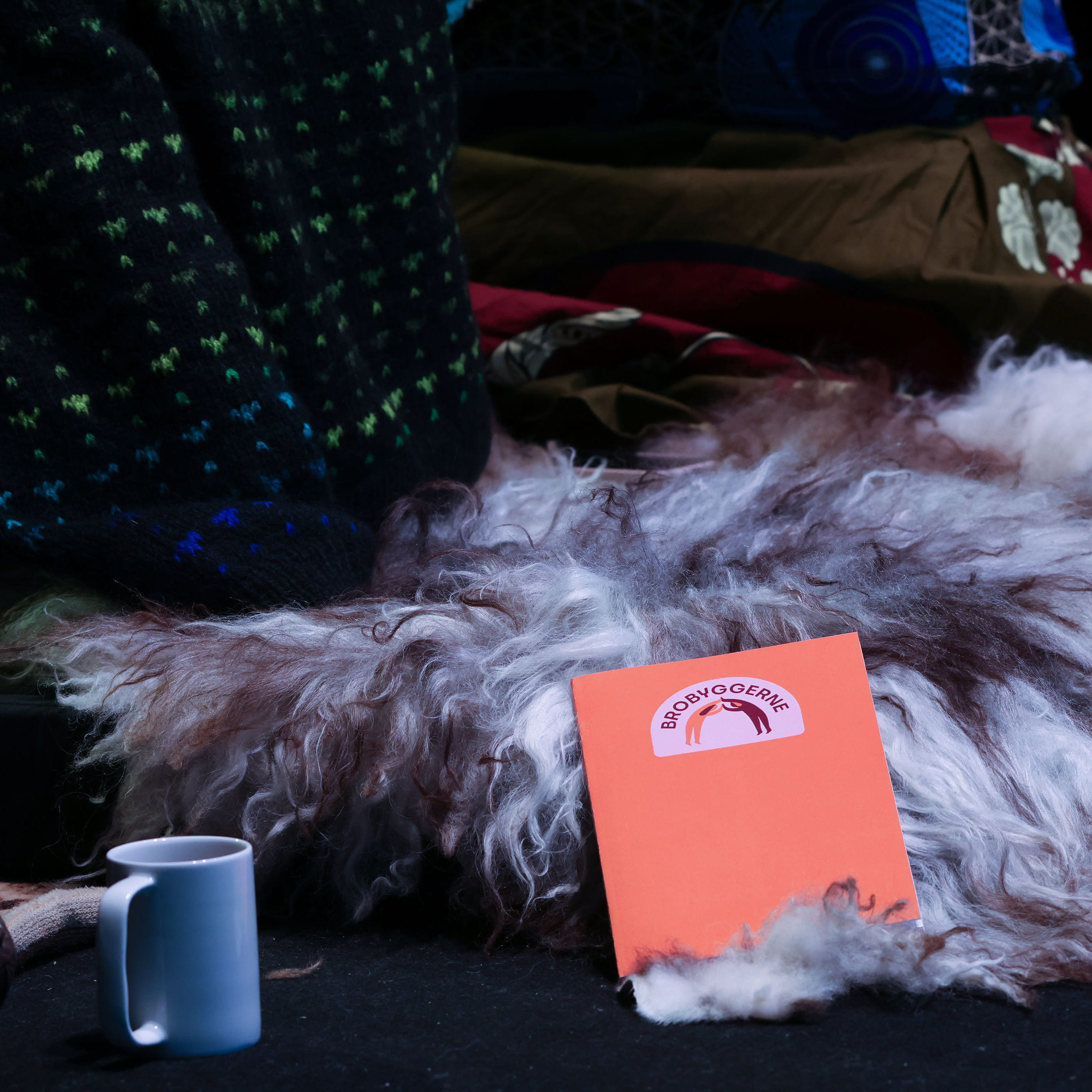 Oransje notatbok med Brobyggerne‑logo ligger på et pelslignende underlag ved siden av en kopp.