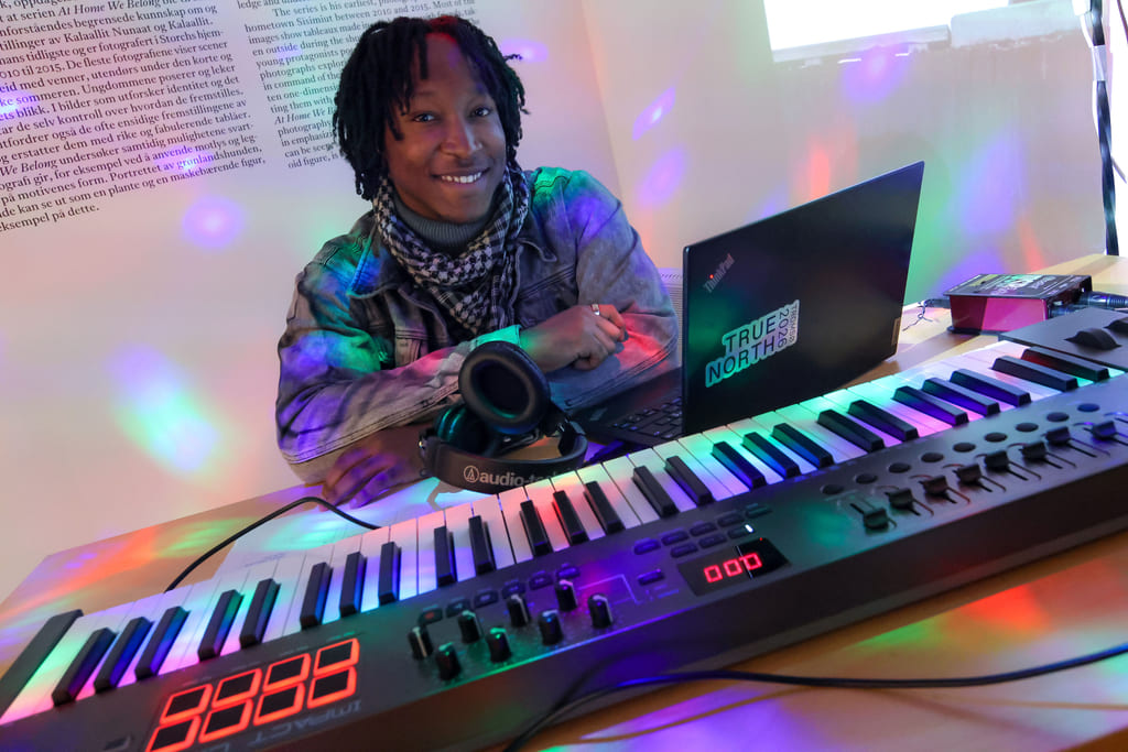 n person sitter ved et keyboard omgitt av farget lys og teknisk utstyr.