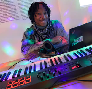 n person sitter ved et keyboard omgitt av farget lys og teknisk utstyr.