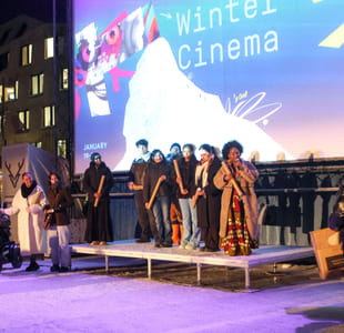 En gruppe mennesker står på en utendørsscene foran en stor skjerm med teksten «Winter Cinema».