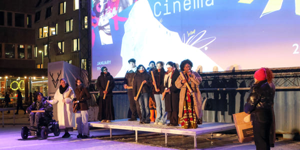 En gruppe mennesker står på en utendørsscene foran en stor skjerm med teksten «Winter Cinema».