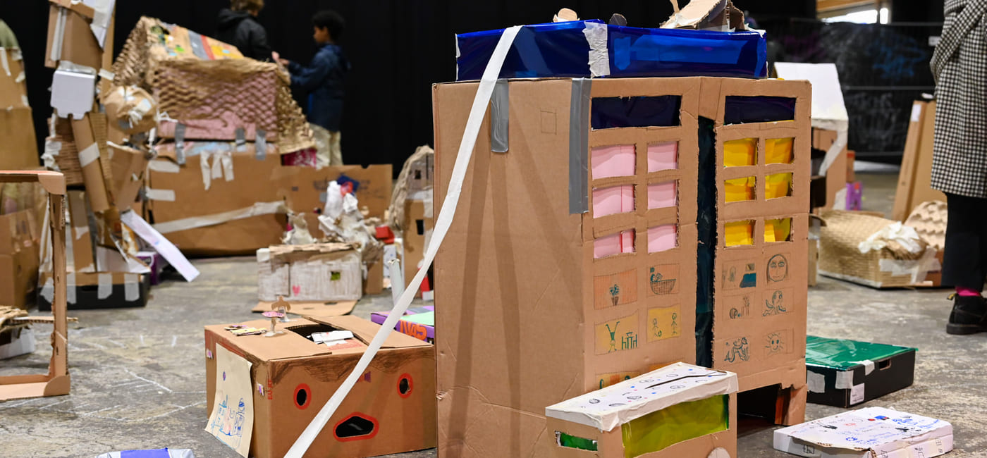 Pappkreasjoner, inkludert bygninger og kjøretøy spredt utover gulvet. Barnekunstprosjekt med esker, tape og fargerik dekorasjon i kreativ montering.