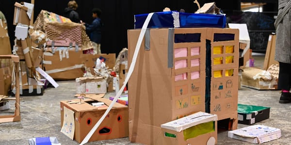 Pappkreasjoner, inkludert bygninger og kjøretøy spredt utover gulvet. Barnekunstprosjekt med esker, tape og fargerik dekorasjon i kreativ montering.