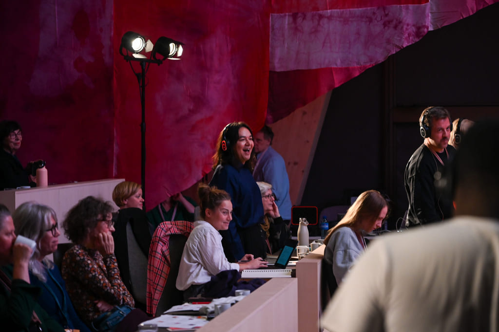 Folk som samhandler i et fargerikt produksjonsstudio eller arrangementslokale med rød bakgrunn og scenebelysning.