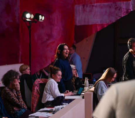 Folk som samhandler i et fargerikt produksjonsstudio eller arrangementslokale med rød bakgrunn og scenebelysning.