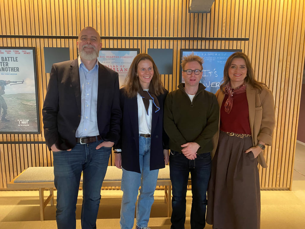 Fire mennesker står oppstilt foran en brun vegg.