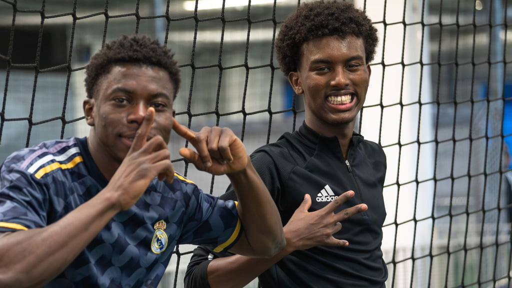 To unge menn smiler mot kamera. De smiler og gestikulerer.