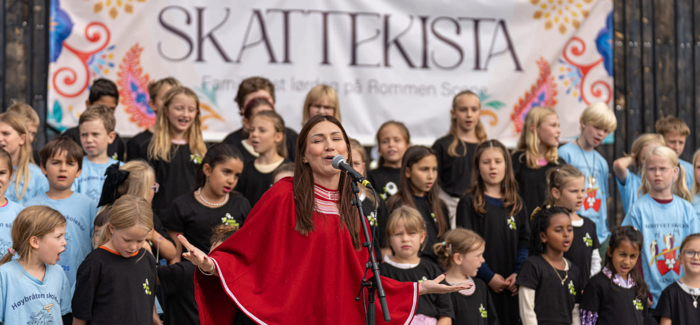 Person står foran en barnekorgruppe med banneret «Skattekista».