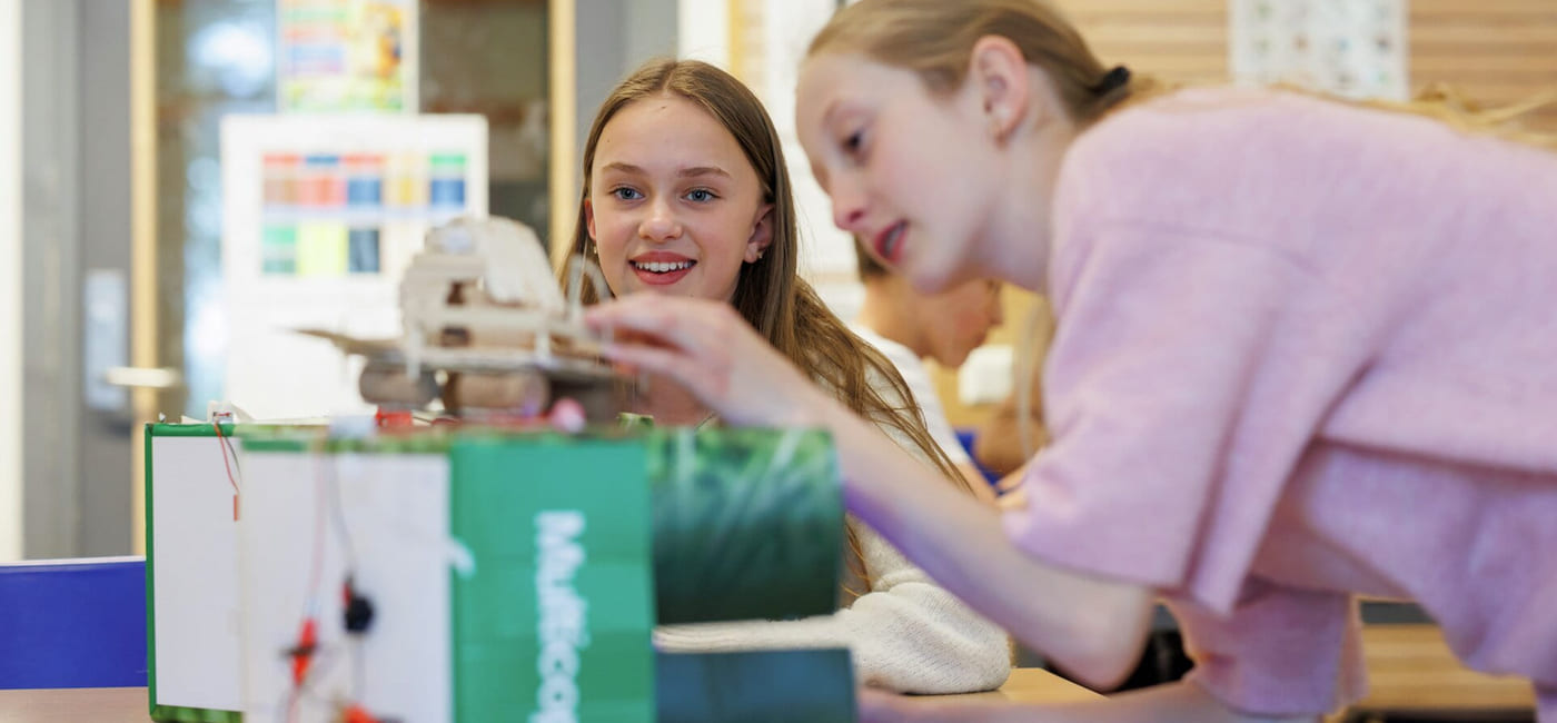 To jenter samarbeider om et STEM-prosjekt med en liten robot eller elektronisk enhet i et klasserom.