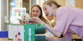 To jenter samarbeider om et STEM-prosjekt med en liten robot eller elektronisk enhet i et klasserom.