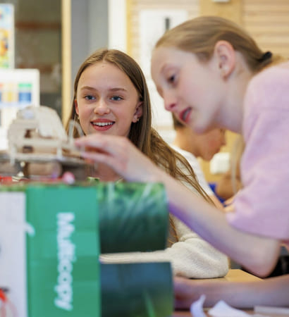 To jenter samarbeider om et STEM-prosjekt med en liten robot eller elektronisk enhet i et klasserom.