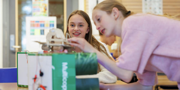 To jenter samarbeider om et STEM-prosjekt med en liten robot eller elektronisk enhet i et klasserom.