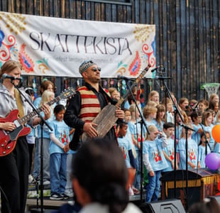 En fargerik parade med folkemengder samlet langs gaten, med et banner over hodet.