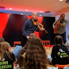 To musikere som spiller fiolin og gitar opptrer for barn som sitter på gulvet på Stovner Skolekor-arrangementet.