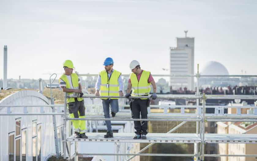 Tre menn på stilas på byggeplass