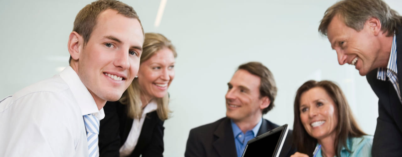 Anerkjennelse: Tre menn og to kvinner i en god situasjon på jobben, samlet rundt et bord.
