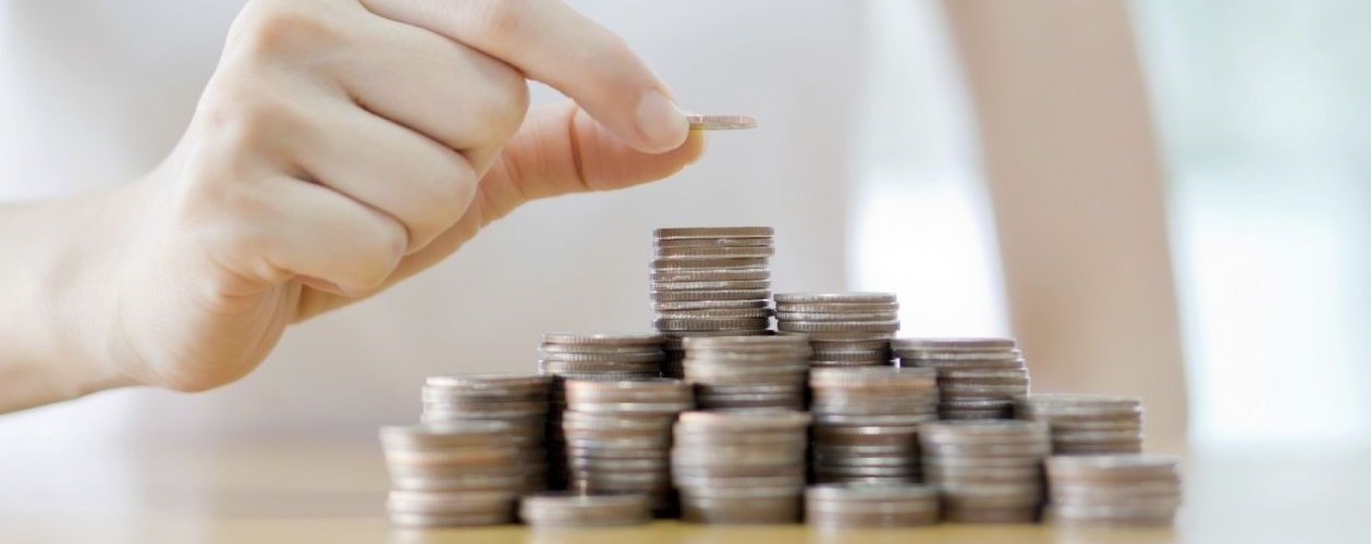 Her ser du en hånd som løfter ett kronestykke på et tårn av andre kronestykker.