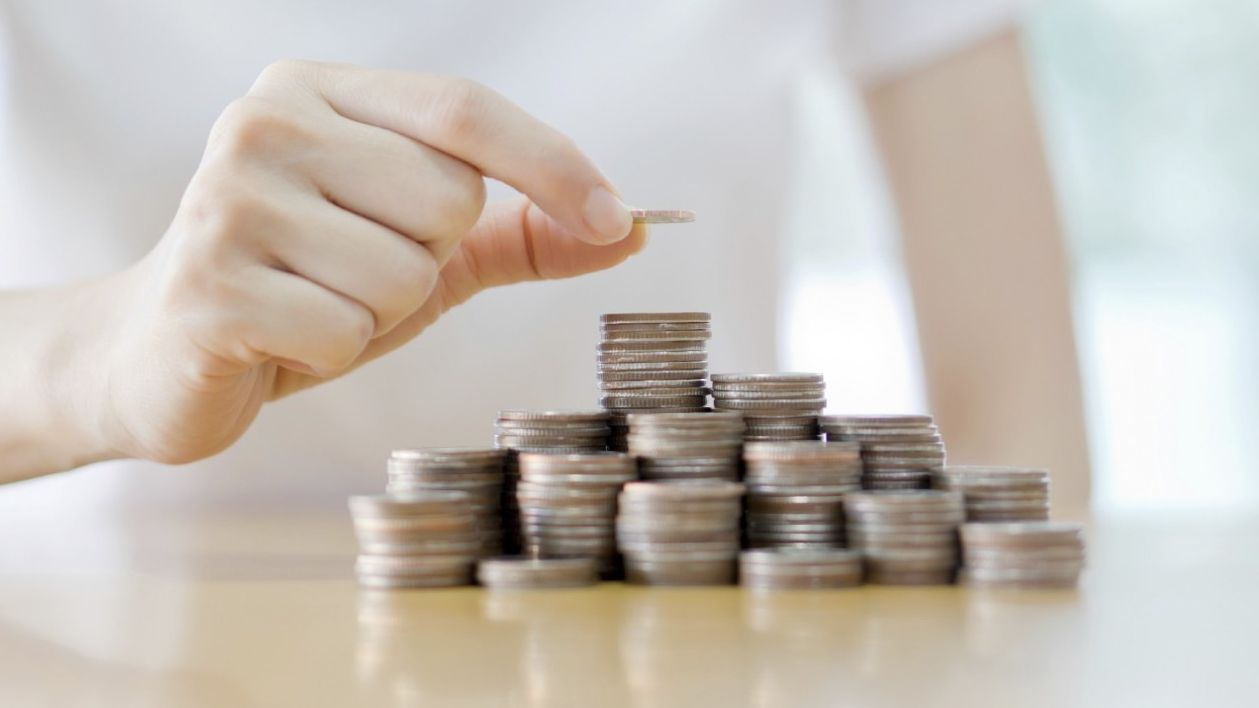 Her ser du en hånd som løfter ett kronestykke på et tårn av andre kronestykker.