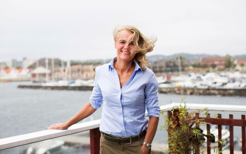 Endring: Blond kvinne står på en veranda med en småbåthavn i bakgrunnen.
