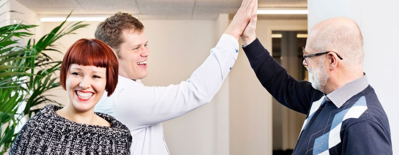 Arbeidsmiljø: To menn gjør «high five», mens en kvinner smiler i forgrunnen.