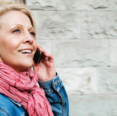 Fleksibel: Blid kvinne snakker i telefonen utendørs.