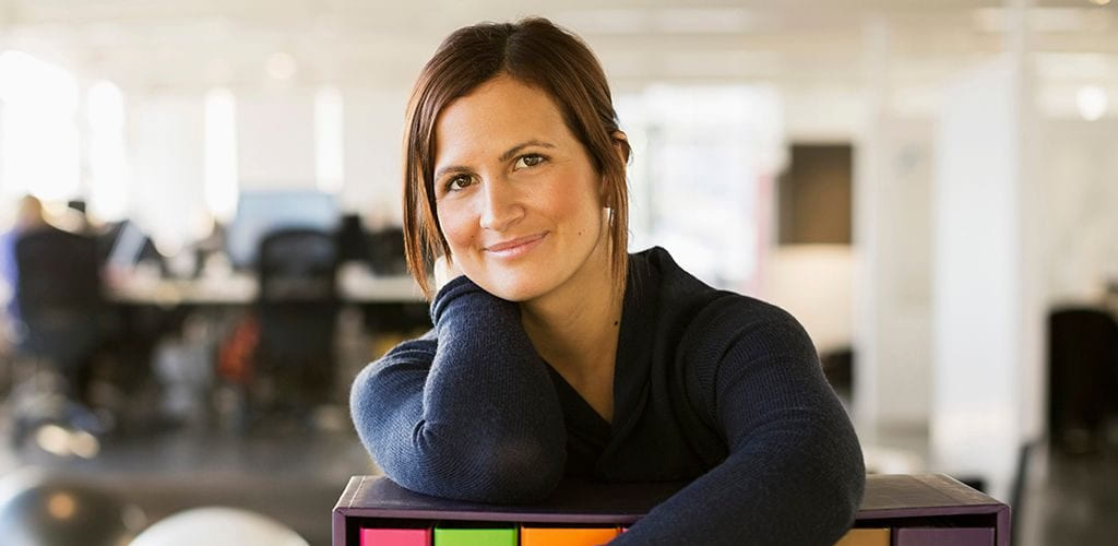 Ledere: Kvinne står lent over en hylle i et kontorlandskap, og smiler til fotografen.