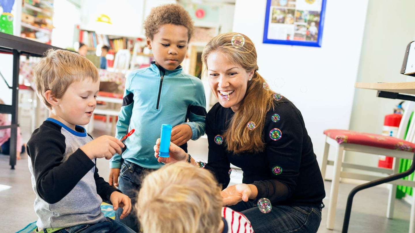 Barnehage: En voksen kvinne og tre barn i samspill i en barnehage.