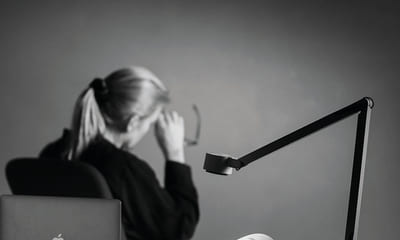 Balanse: Kvinne sitter vendt bort fra skrivebordet sitt og det ligger en maske på bordet med hennes smilende fjes på.