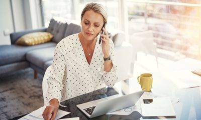 en kvinne har hjemmekontor. Snakker i telefonen foran laptop.