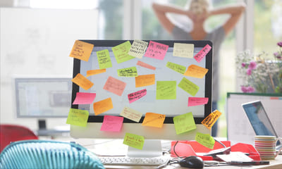 Dataskjerm med mange post-its, illustrerer mange oppgaver og behovet for å prioritere