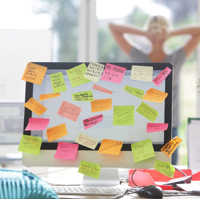 Dataskjerm med mange post-its, illustrerer mange oppgaver og behovet for å prioritere