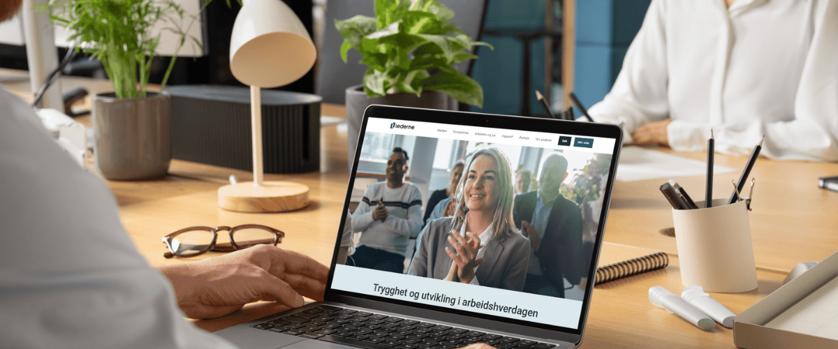 To personer sitter på kontor, og Ledernes hjemmeside vises på pc