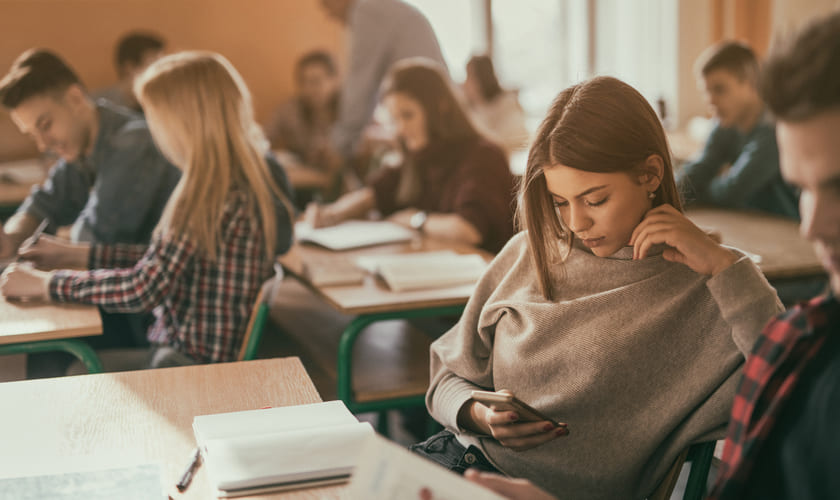 En elev ser på telefonen i timen. Bilde.