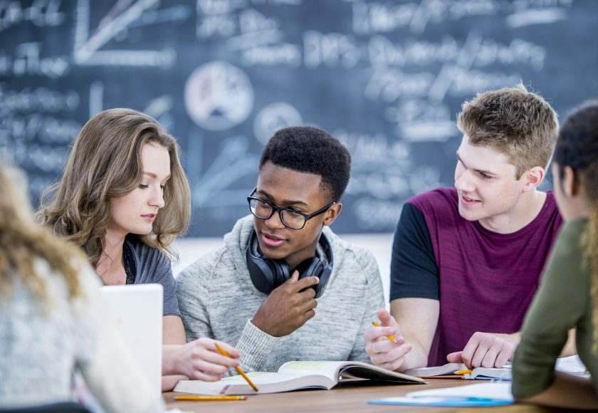 En gruppe studenter sitter ved et bord i et klasserom og løser oppgaver sammen. Bilde.