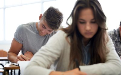 To ungdommer sitter og skriver i et klasserom. Bilde.
