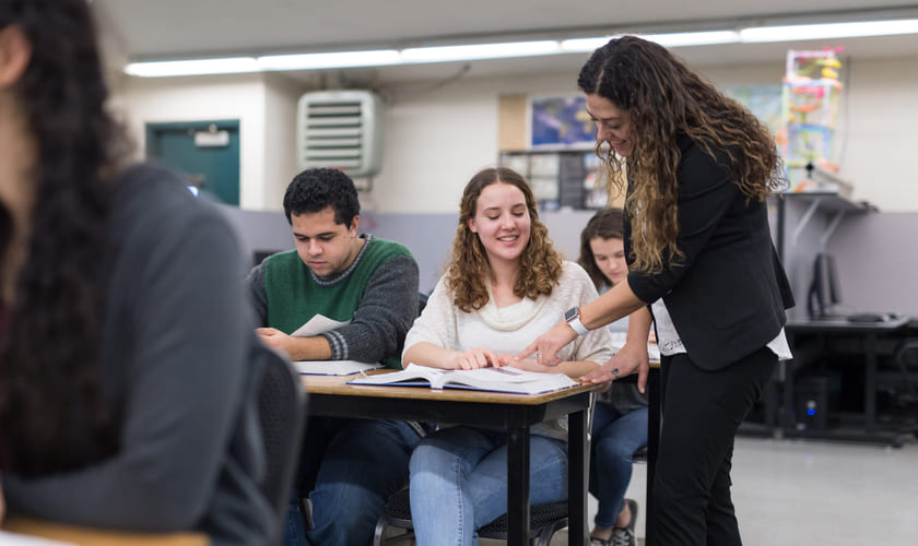 Illustrasjonsbilde av en lærer som hjelper en videregåendeelev i klasserommet med noe i en bok.