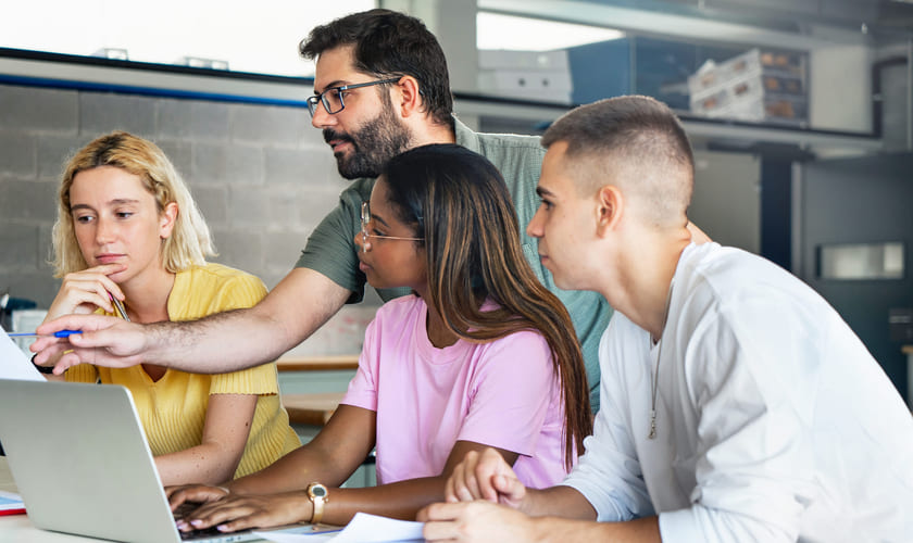 En lærer hjelper elever med noe på en laptop-skjerm. Bilde.