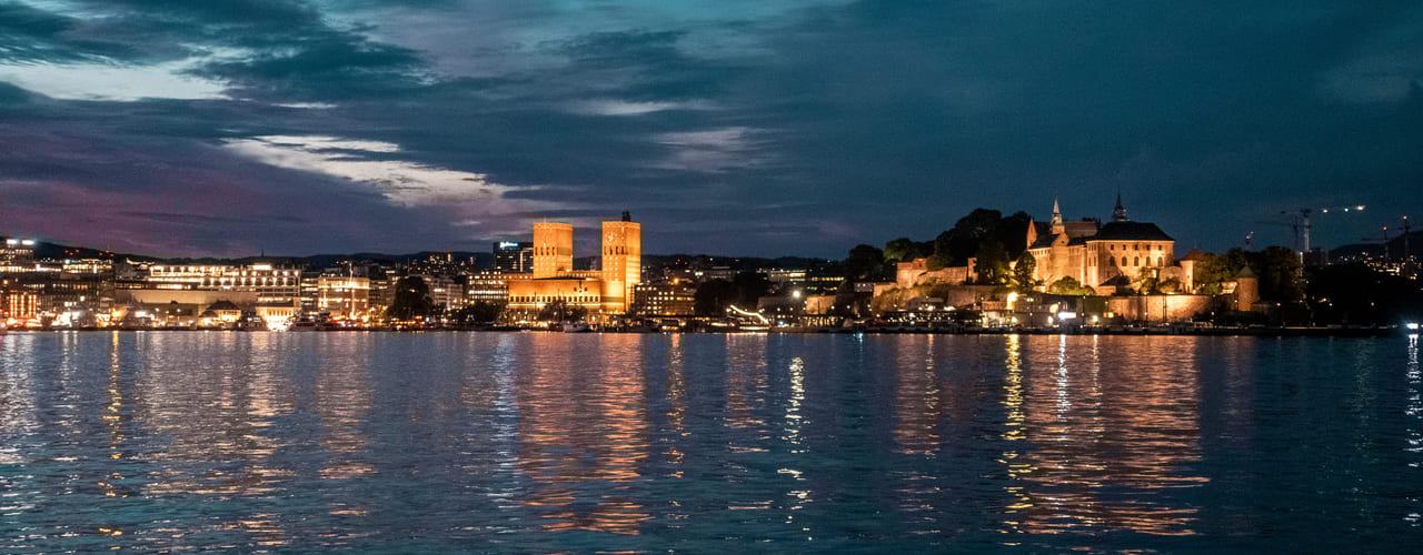 Oslo rådhus og Akershus festning sett fra fjorden om kvelden. Bilde.