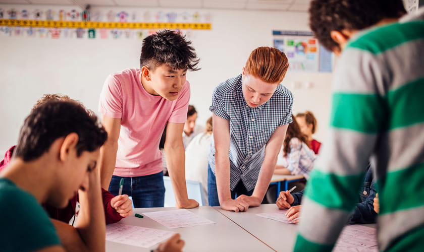 Fire elever rundt et bord i et klasserom. Bilde.