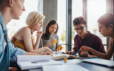 Studenter diskuterer rundt et bord. Bilde.