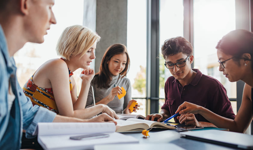 Studenter diskuterer rundt et bord. Bilde.