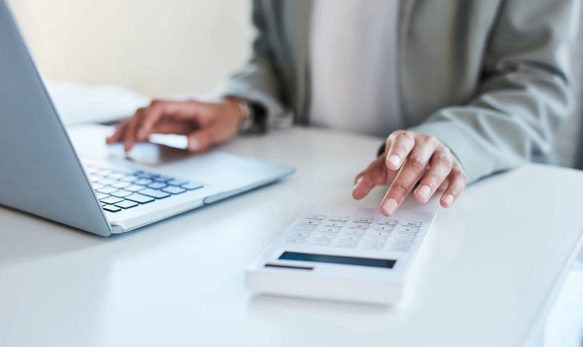 Dame sitter ved skrivebord med laptop og kalkulator. Illustrasjonsbilde.