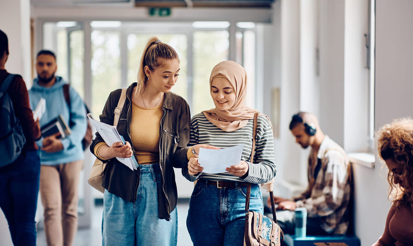 To jenter på videregående står i en gang og sammenlikner notater. Bilde.